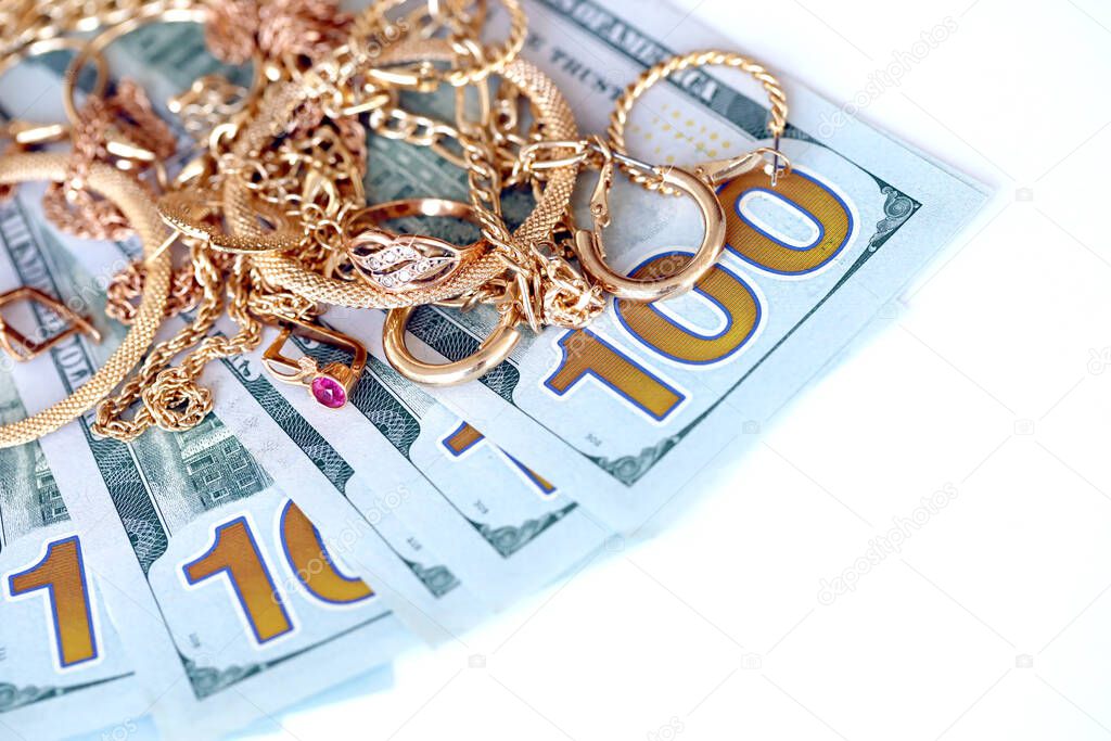 Many expensive golden jewerly rings, earrings and necklaces with big amount of US dollar bills on white background. Pawnshop or jewerly shop concept
