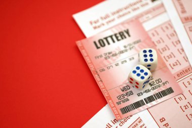 Red lottery ticket with dice lies on pink gambling sheets with numbers for marking to play lottery. Lottery playing concept or gambling addiction. Close up photo