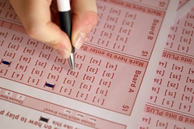 Filling out a lottery ticket. A young woman plays the lottery and dreams of winning the jackpot. Female hand marking number on red lottery ticket close up