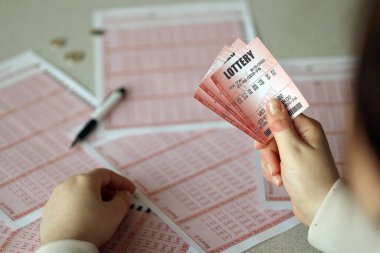 Filling out a lottery ticket. A young woman holds the lottery ticket with complete row of numbers on the lottery blank sheets background. Gambling concept