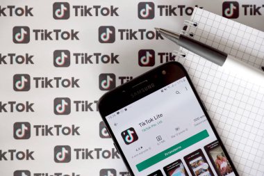 TERNOPIL, UKRAINE - 2 Mayıs 2022: Tik Tok akıllı telefon uygulaması ekranda ve birçok TikTok logosu kağıda basıldı. Tiktok veya Douyin, ByteDance Ltd. 'nin sahibi olduğu Çin yapımı kısa formatlı video sunucu servisidir.