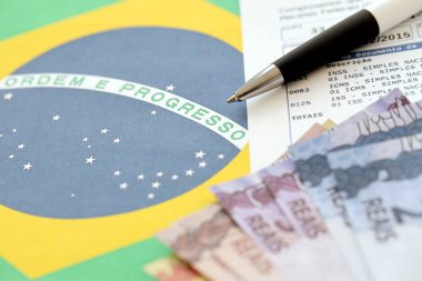 TERNOPIL, UKRAINE - 20 Mayıs 2022: Brezilya tahsilat raporunun Brezilya reel paraları ve ulusal bayrak arka planında kalem ile kanıtlanması. Brezilya 'nın yasal vergi ödeme ve vergi raporlama kavramı