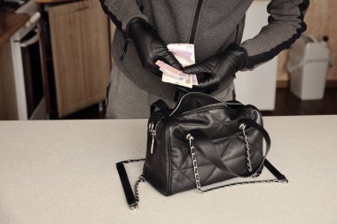 Siyah kıyafetli ve eldivenli soyguncu, çalıntı kadın çantasının içini görmüş. Hırsız, Ukrayna 'nın parasını mutfaktaki bir kadın çantasından almış.