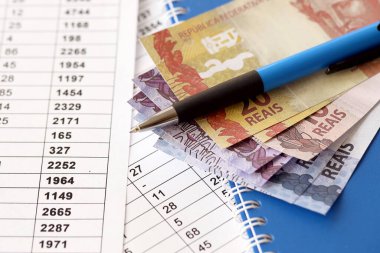 Pen with Brazilian money bills on documents with calculations table. Concept of business, accounting or taxpaying in Brazil clipart
