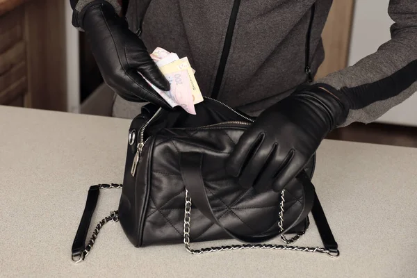 Siyah kıyafetli ve eldivenli soyguncu, çalıntı kadın çantasının içini görmüş. Hırsız, Ukrayna 'nın parasını mutfaktaki bir kadın çantasından almış.