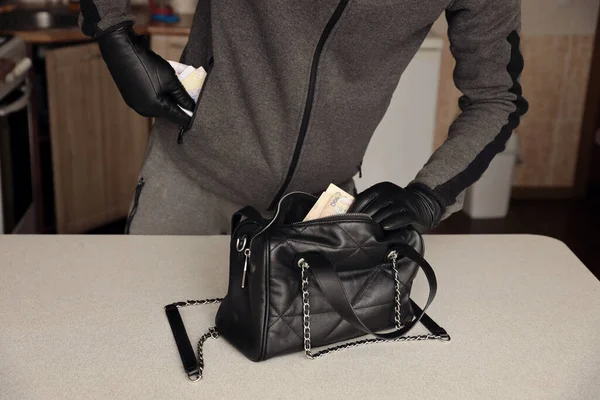 Siyah kıyafetli ve eldivenli soyguncu, çalıntı kadın çantasının içini görmüş. Hırsız, Ukrayna 'nın parasını mutfaktaki bir kadın çantasından almış.