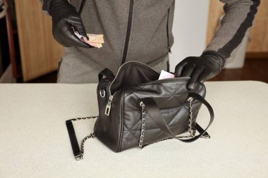 Siyah kıyafetli ve eldivenli soyguncu, çalıntı kadın çantasının içini görmüş. Hırsız, Ukrayna 'nın parasını mutfaktaki bir kadın çantasından almış.