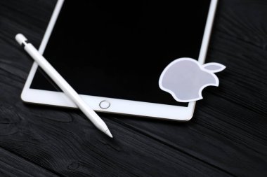 KHARKIV, UKRAINE - JANUARY 27, 2021: Brand new Apple iPad and Apple Pencil and gray company logo on black background. Apple Inc. is an American technology company headquartered in California