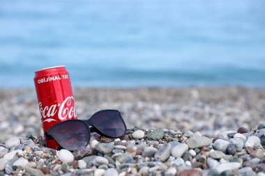 ANTALYA, TURKEY - 18 Mayıs 2021: Orijinal Coca Cola kırmızı teneke kutu deniz kıyısına yakın küçük yuvarlak çakıl taşları üzerinde yatar. Türk sahilinde Coca-Cola kutusu ve güneş gözlüğü