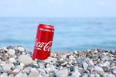ANTALYA, TURKEY - 18 Mayıs 2021: Orijinal Coca Cola kırmızı teneke kutu deniz kıyısına yakın küçük yuvarlak çakıl taşları üzerinde yatar. Türk plaj taşları üzerinde Coca-Cola