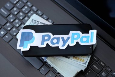 TERNOPIL, UKRAINE - SEPTEMBER 6, 2022 Paypal paper logotype lies on black laptop keyboard with US dollar bills. Payoneer is American financial services company provides online money transfer