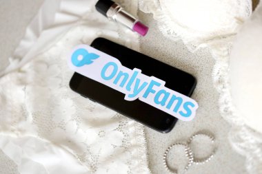 TERNOPIL, UKRAINE - SEPTEMBER 6, 2022 Onlyfans paper logotype among lipstick, earrings and women lingerie close to black smartphone