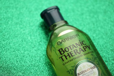 TERNOPIL, UKRAINE - SEPTEMBER 2, 2022 Bottle of Garnier Botanic Therapy Green Tea Shampoo on green glitter background surface