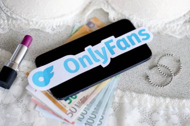 TERNOPIL, UKRAINE - SEPTEMBER 6, 2022 Onlyfans paper logotype among lipstick, earrings and women lingerie close to bunch of few euro bills