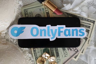 TERNOPIL, UKRAINE - SEPTEMBER 6, 2022 Onlyfans paper logotype among lipstick, earrings and women lingerie close to bunch of few US dollar bills