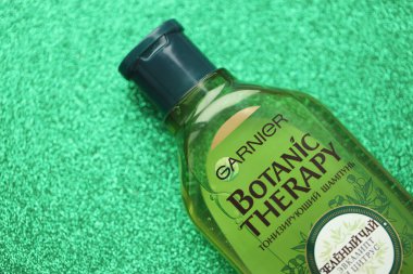 TERNOPIL, UKRAINE - SEPTEMBER 2, 2022 Bottle of Garnier Botanic Therapy Green Tea Shampoo on green glitter background surface
