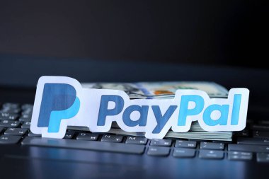 TERNOPIL, UKRAINE - SEPTEMBER 6, 2022 Paypal paper logotype lies on black laptop keyboard with US dollar bills. Payoneer is American financial services company provides online money transfer