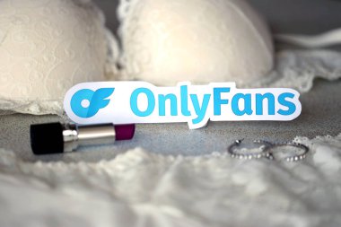 TERNOPIL, UKRAINE - SEPTEMBER 6, 2022 Onlyfans paper logotype among lipstick, earrings and women lingerie close up