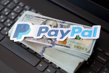 TERNOPIL, UKRAINE - SEPTEMBER 6, 2022 Paypal paper logotype lies on black laptop keyboard with US dollar bills. Payoneer is American financial services company provides online money transfer