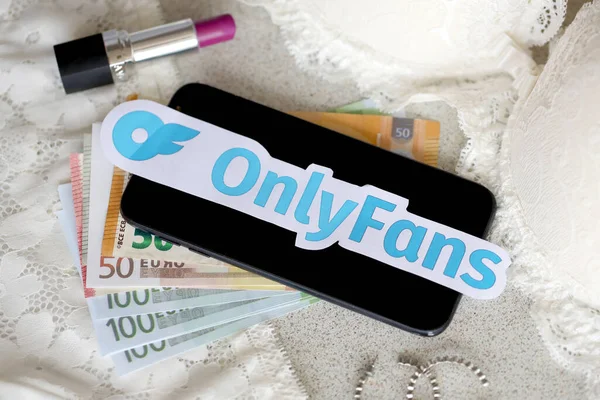 TERNOPIL, UKRAINE - SEPTEMBER 6, 2022 Onlyfans paper logotype among lipstick, earrings and women lingerie close to bunch of few euro bills