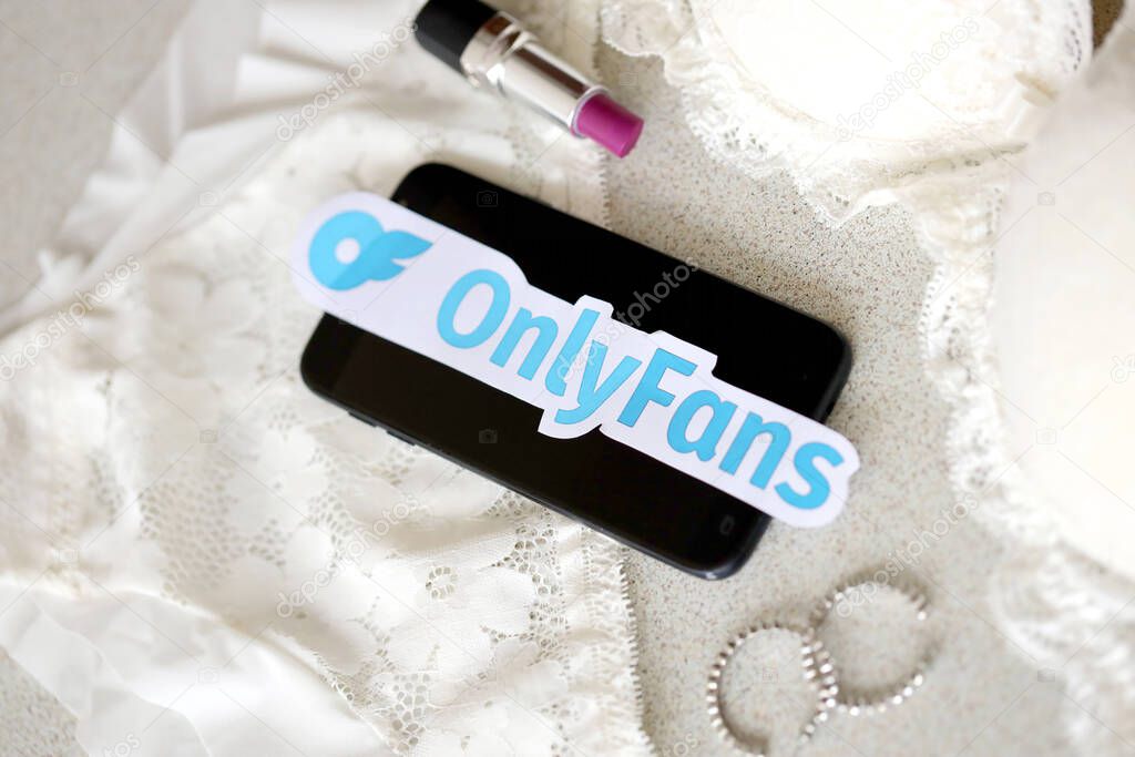 TERNOPIL, UKRAINE - SEPTEMBER 6, 2022 Onlyfans paper logotype among lipstick, earrings and women lingerie close to black smartphone
