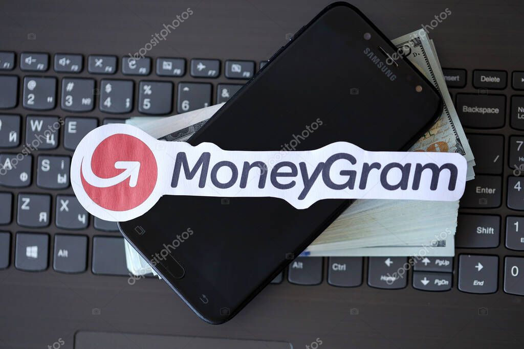 TERNOPIL, UKRAINE - SEPTEMBER 6, 2022 MoneyGram paper logotype lies on black laptop keyboard with US dollar bills. Moneygram is American cross border P2P payments and money transfer company