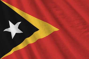 Büyük kıvrımlı Timor Leste bayrağı stüdyo ışıklarının altında sallanıyor. Resmi semboller ve renkler kumaş pankartıyla
