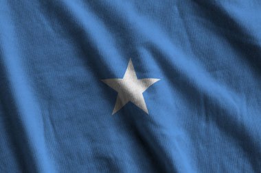Stüdyo ışıklarının altında büyük kıvrımlı Somali bayrağı sallanıyor. Resmi semboller ve renkler kumaş pankartıyla