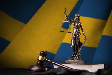 İsveç bayrağı, kadın adaleti heykeli, anayasa ve siyah kumaş üzerinde yargıç çekici. Hüküm ve ceza kavramı