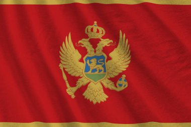 Stüdyo ışıklarının altında büyük kıvrımlı Karadağ bayrağı sallanıyor. Resmi semboller ve renkler kumaş pankartıyla