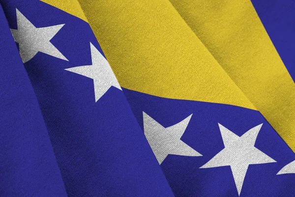 Bosnia and Herzegovina flag with big folds waving close up under the studio light indoors. The official symbols and colors in fabric banner