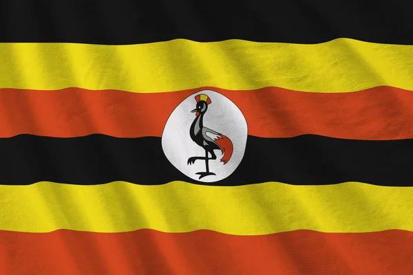 Uganda flag with big folds waving close up under the studio light indoors. The official symbols and colors in fabric banner