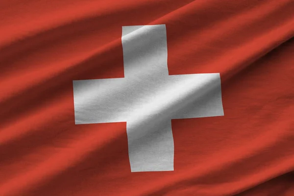 Switzerland flag with big folds waving close up under the studio light indoors. The official symbols and colors in fabric banner