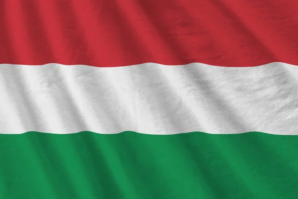 Hungary flag with big folds waving close up under the studio light indoors. The official symbols and colors in fabric banner