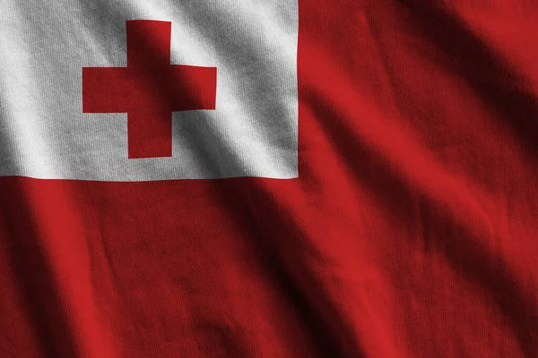 Tonga flag with big folds waving close up under the studio light indoors. The official symbols and colors in fabric banner