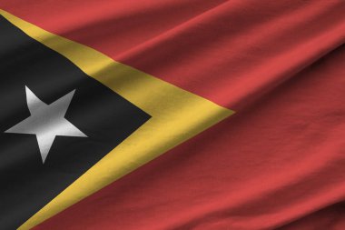 Büyük kıvrımlı Timor Leste bayrağı stüdyo ışıklarının altında sallanıyor. Resmi semboller ve renkler kumaş pankartıyla