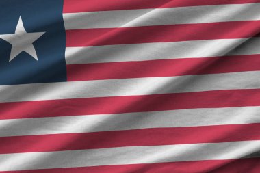 Stüdyo ışıklarının altında büyük kıvrımlı Liberya bayrağı sallanıyor. Resmi semboller ve renkler kumaş pankartıyla