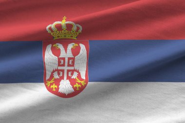 Stüdyo ışıklarının altında büyük kıvrımlı Sırbistan bayrağı sallanıyor. Resmi semboller ve renkler kumaş pankartıyla
