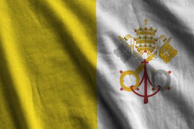 Vatikan Şehri bayrağı. Stüdyo ışıklarının altında büyük kıvrımlar sallanıyor. Resmi semboller ve renkler kumaş pankartıyla