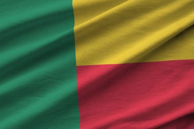 Stüdyo ışıklarının altında büyük kıvrımlı Benin bayrağı sallanıyor. Resmi semboller ve renkler kumaş pankartıyla