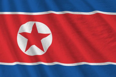 Büyük kıvrımlı Kuzey Kore bayrağı stüdyo ışıklarının altında sallanıyor. Resmi semboller ve renkler kumaş pankartıyla