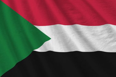 Büyük kıvrımlı Sudan bayrağı stüdyo ışıklarının altında sallanıyor. Resmi semboller ve renkler kumaş pankartıyla