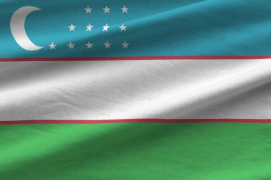 Stüdyo ışıklarının altında büyük kıvrımlı Özbekistan bayrağı sallanıyor. Resmi semboller ve renkler kumaş pankartıyla