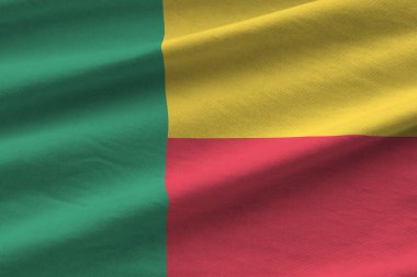 Stüdyo ışıklarının altında büyük kıvrımlı Benin bayrağı sallanıyor. Resmi semboller ve renkler kumaş pankartıyla