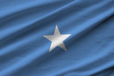 Stüdyo ışıklarının altında büyük kıvrımlı Somali bayrağı sallanıyor. Resmi semboller ve renkler kumaş pankartıyla