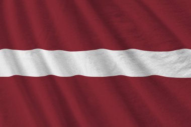 Büyük kıvrımlı Letonya bayrağı stüdyo ışıklarının altında sallanıyor. Resmi semboller ve renkler kumaş pankartıyla