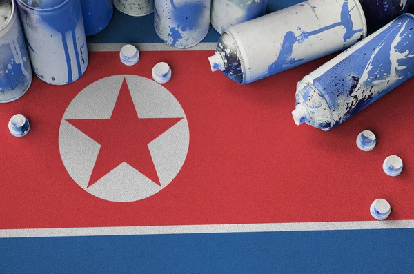 North Korea flag and few used aerosol spray cans for graffiti painting. Street art culture concept, vandalism problems