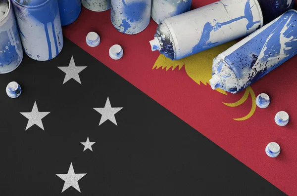 Papua New Guinea flag and few used aerosol spray cans for graffiti painting. Street art culture concept, vandalism problems