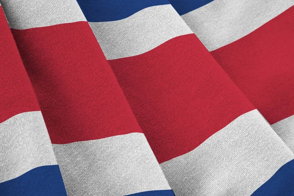 Costa Rica flag with big folds waving close up under the studio light indoors. The official symbols and colors in fabric banner