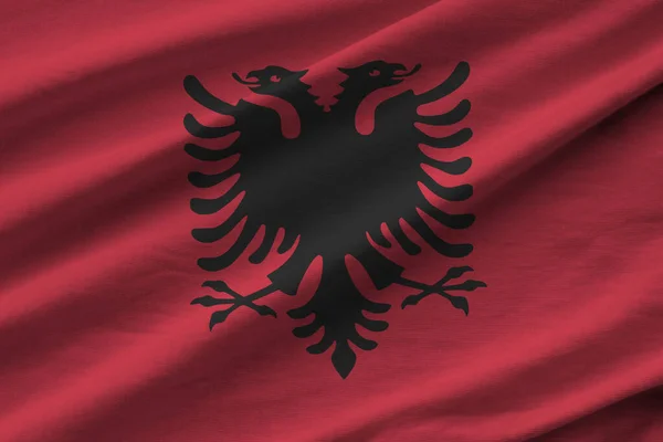 Albania flag with big folds waving close up under the studio light indoors. The official symbols and colors in fabric banner